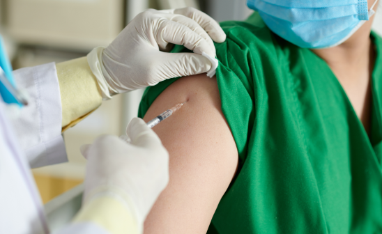 Profesional de la salud administrando una vacuna en el brazo de un paciente con guantes y mascarilla - LaCardio