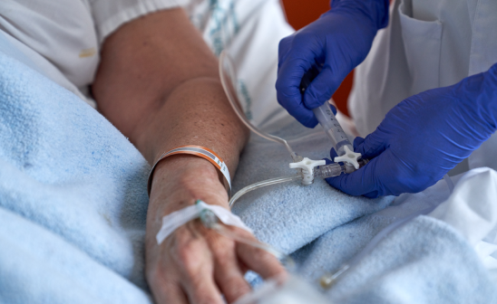 Mano de paciente con vía intravenosa mientras un profesional de la salud ajusta la conexión con guantes azules - LaCardio